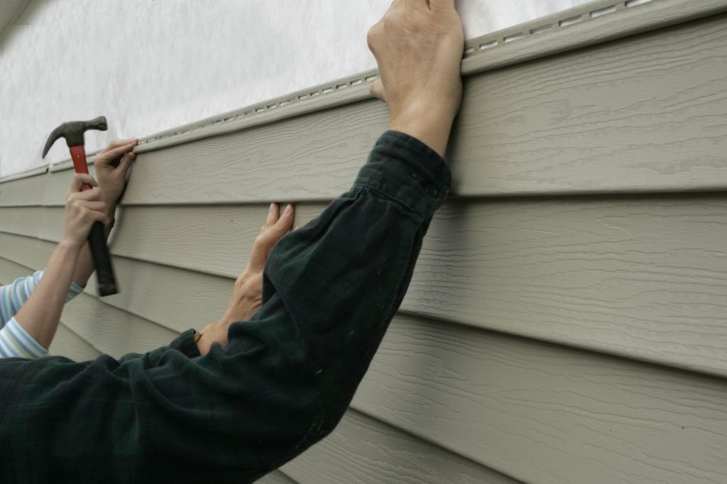 Contractor repairing cracked house siding on Minnesota home after weather-related exterior damage